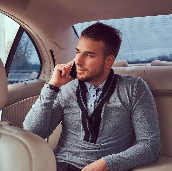 Foto di un uomo che guarda fuori dal finestrino di una vettura dagli interni di pelle mentre parla al telefono.