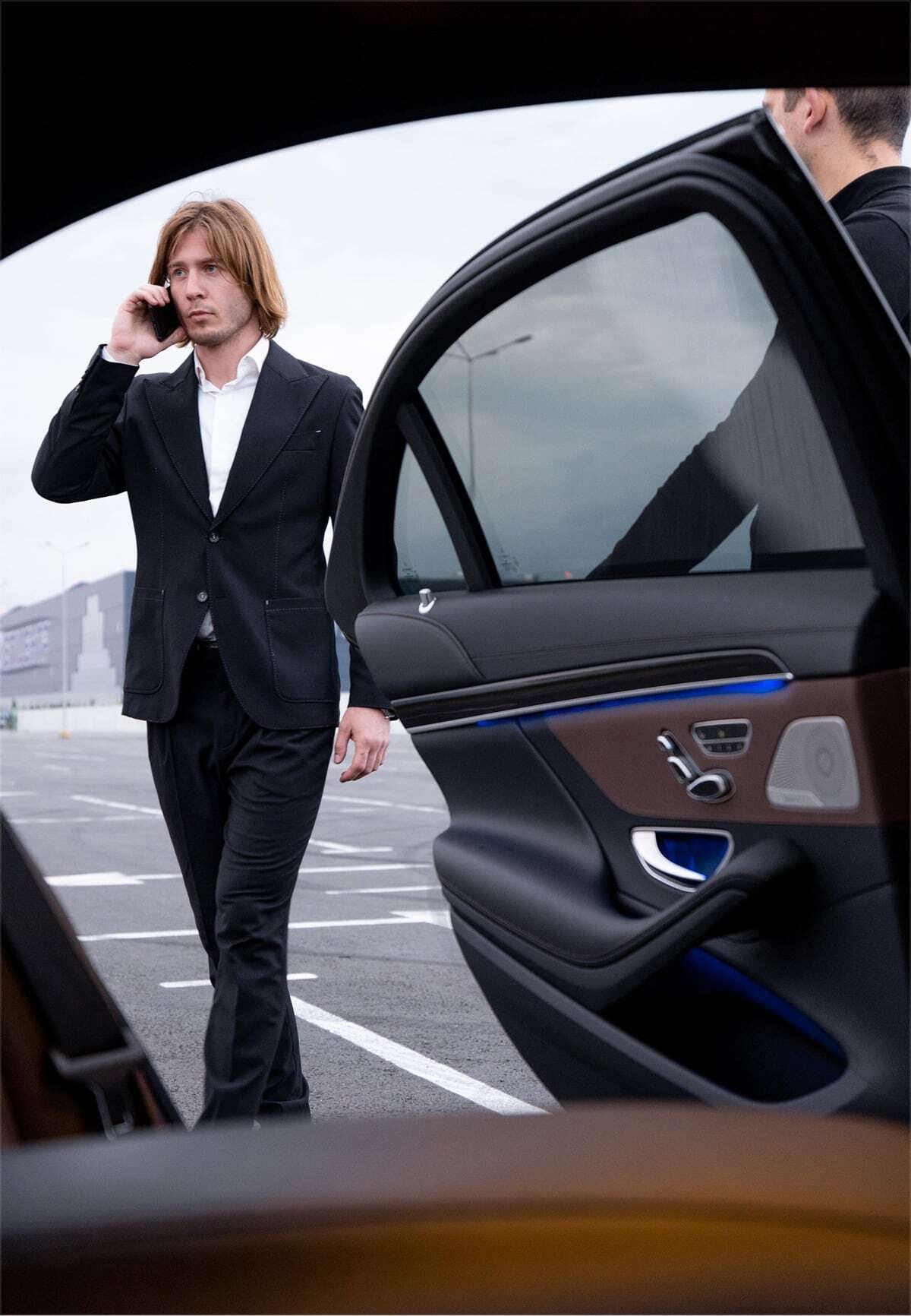 Foto di un uomo al telefono entra in una vettura di rappresentanza mentre l'autista gli tiene aperta la portiera